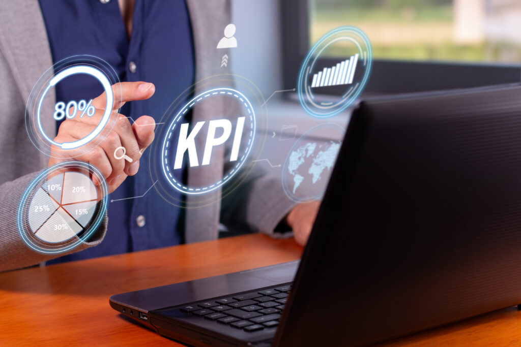 Osoba analizuje KPI w sprzedaży B2B na laptopie i ekranie z podstawowymi wskaźnikami wyników.